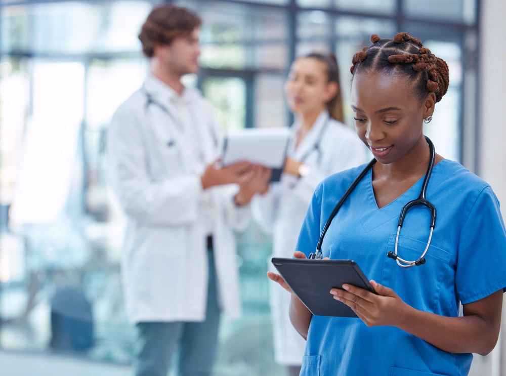 medical assistant in foreground using tablet with practitioners conversing in background